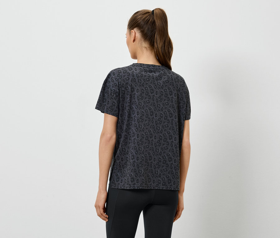 Frau mit Pferdeschwanz trägt ein gemustertes, dunkles T-Shirt und Leggings, von hinten gesehen.