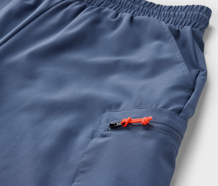 Detailaufnahme einer blauen, packbaren Shorts mit orangefarbenem Reißverschluss an der Tasche.