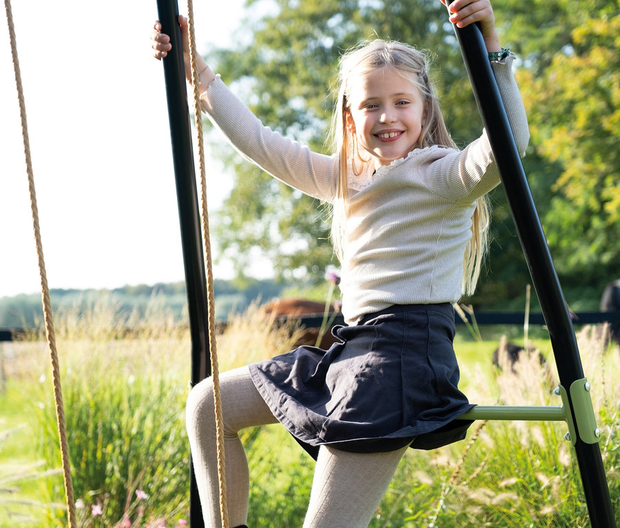 Ein Mädchen lächelt und hält sich am Rahmen der EXIT Doppelschaukel »Ivy« fest.
