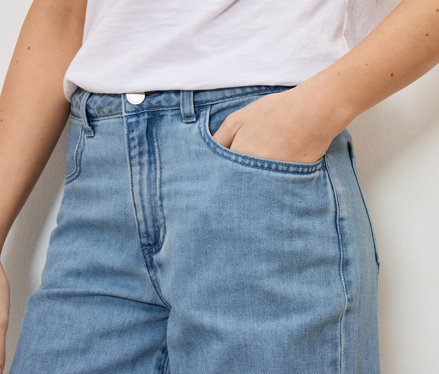 Nahaufnahme einer Frau, die hellblaue Jeans und ein weißes T-Shirt trägt und ihre Hand in die Hosentasche steckt.