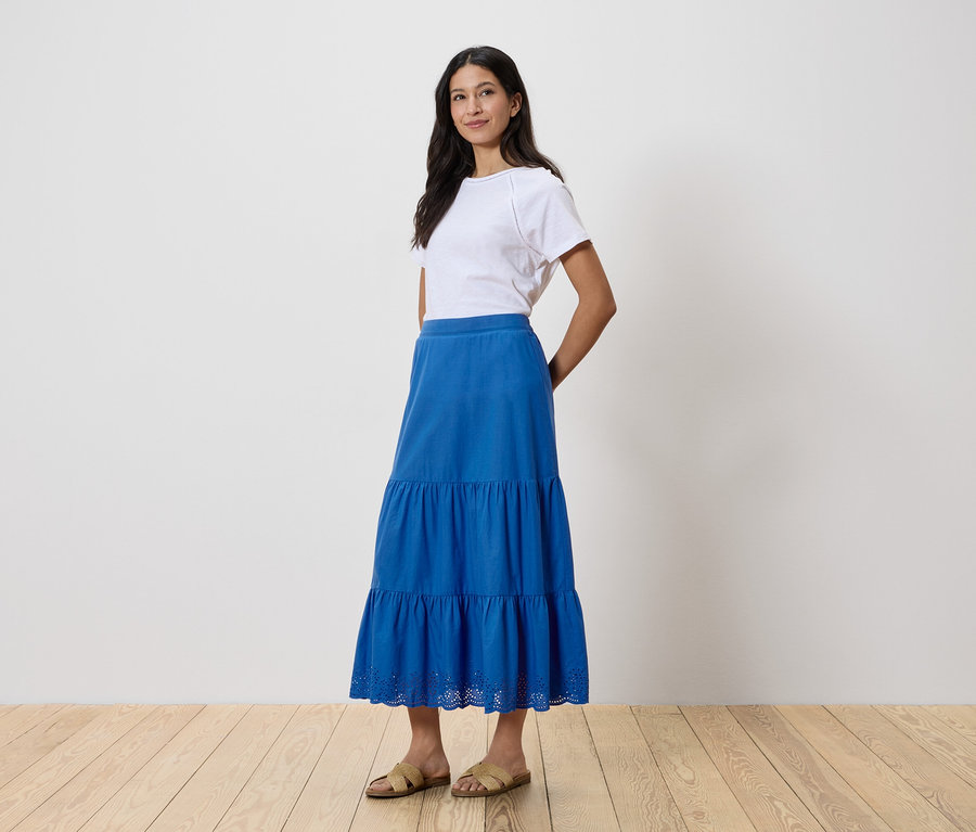 Frau steht und trägt ein weißes T-Shirt und einen blauen Rock.