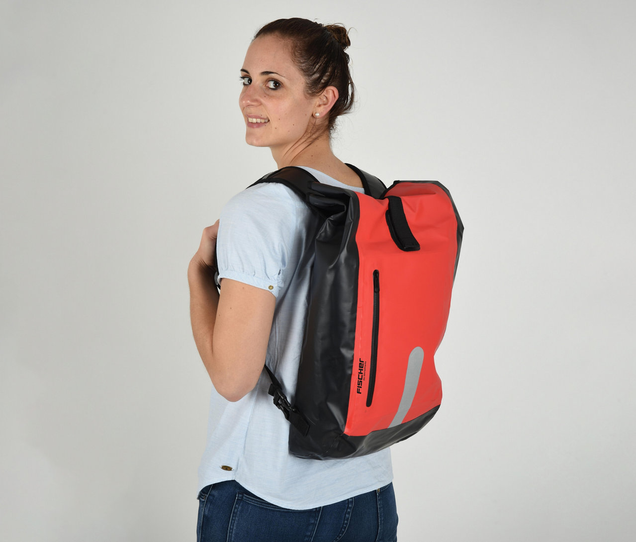 Frau mit FISCHER wasserdichter Gepäckträgertasche in rot und schwarz auf dem Rücken, blickt über die Schulter.