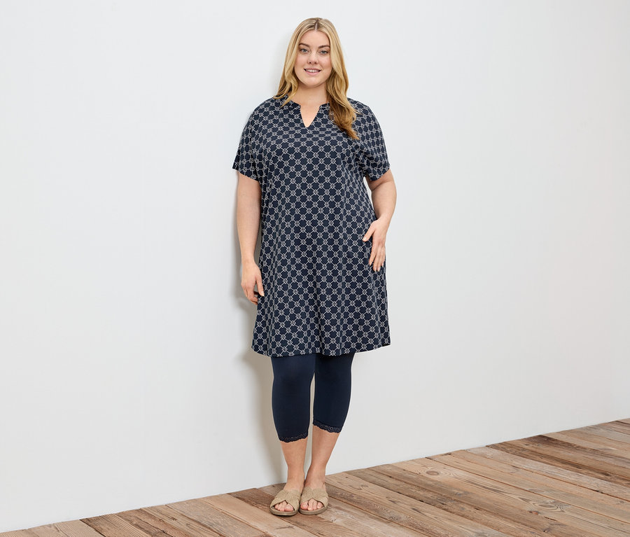 Frau in einem gemusterten Kleid mit dunkelblauen 3/4-Leggings mit Spitzenborte.