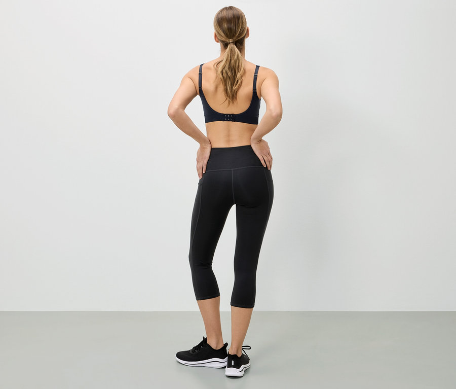 Frau von hinten in Sport-BH, schwarzen Tights und Turnschuhen, die ihre Hände auf die Hüften legt.