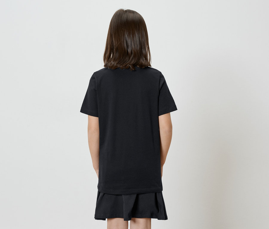 Kind mit dunklen, schulterlangen Haaren von hinten, trägt ein schwarzes T-Shirt und einen schwarzen Rock vor einem neutralen Hintergrund.