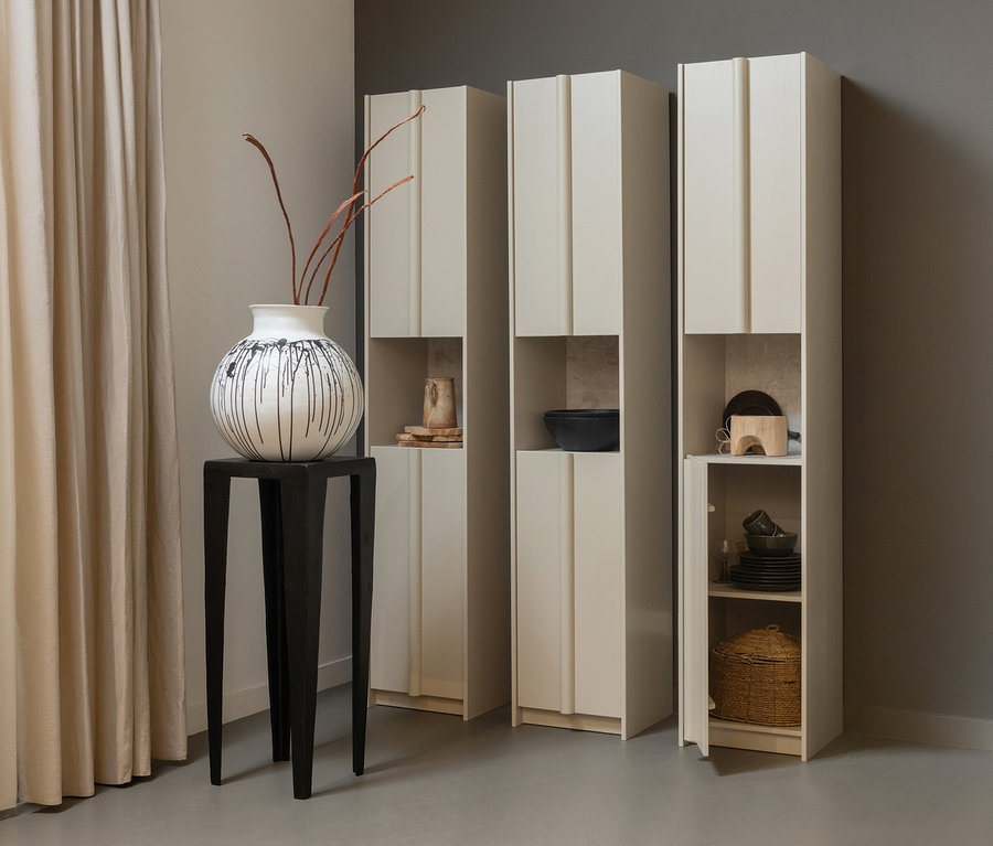 Drei WOOOD »Basu« Schränke in Kiefer Dust stehen neben einem schwarzen Tisch mit einer Vase und Ästen.