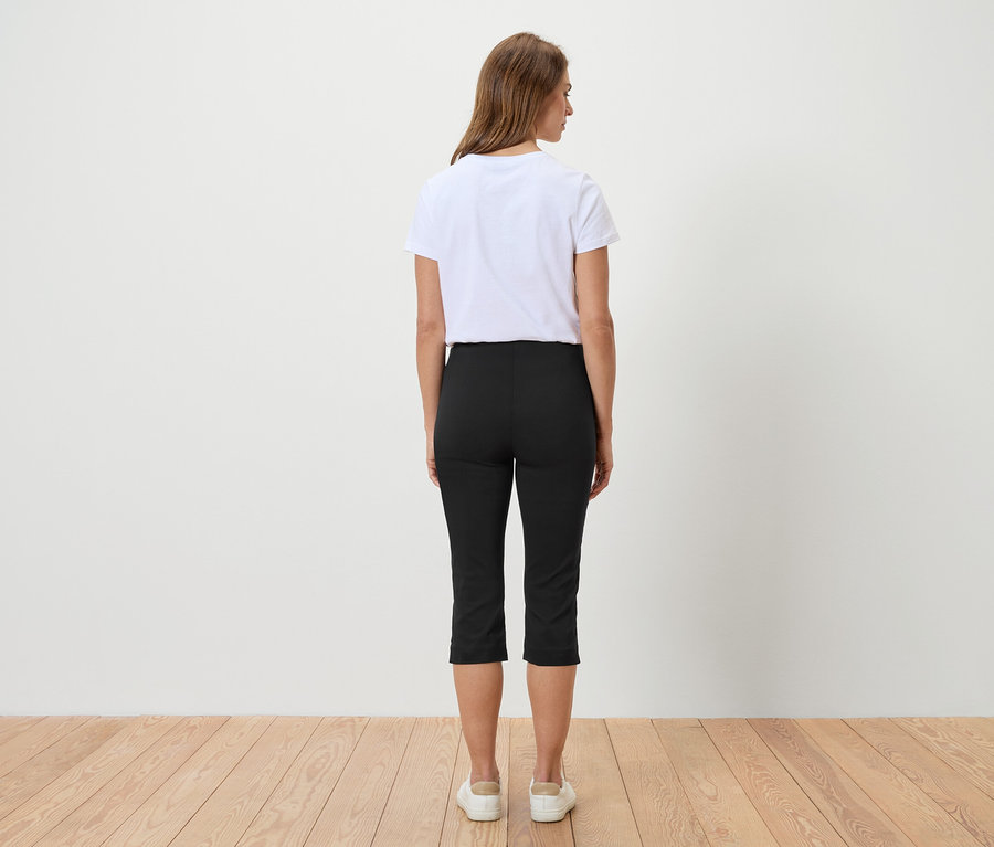 Rückansicht einer Frau mit braunen Haaren, die ein weißes T-Shirt, eine schwarze Caprihose und weiße Turnschuhe trägt.
