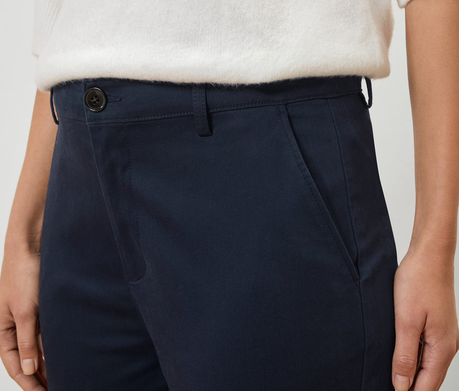 Nahaufnahme einer Person, die eine marineblaue Hose und einen weißen Pullover trägt.