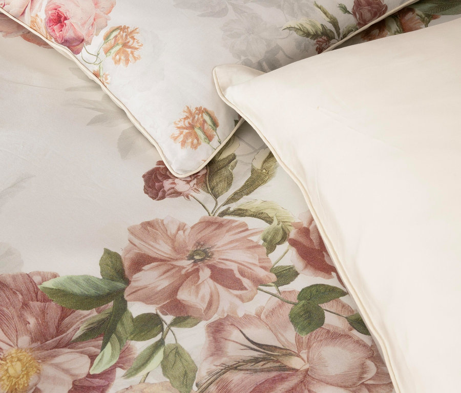 Nahaufnahme von Bettwäsche mit Blumenmuster und einem weißen Kissen.