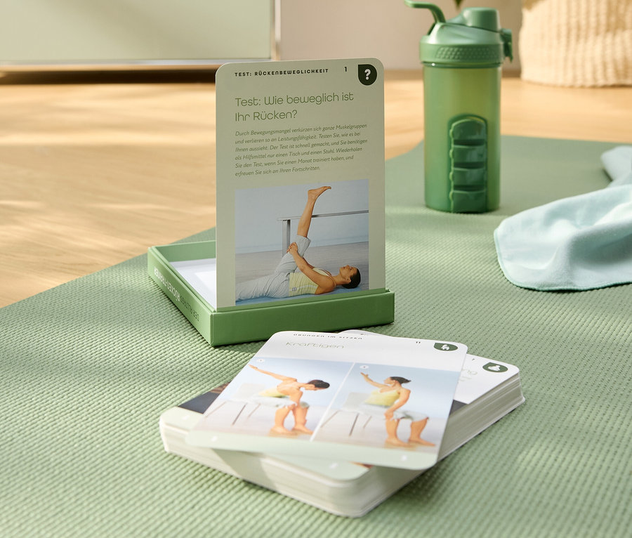 Auf einer grünen Yogamatte liegen Übungskarten, eine grüne Trinkflasche und ein grünes Kästchen.
