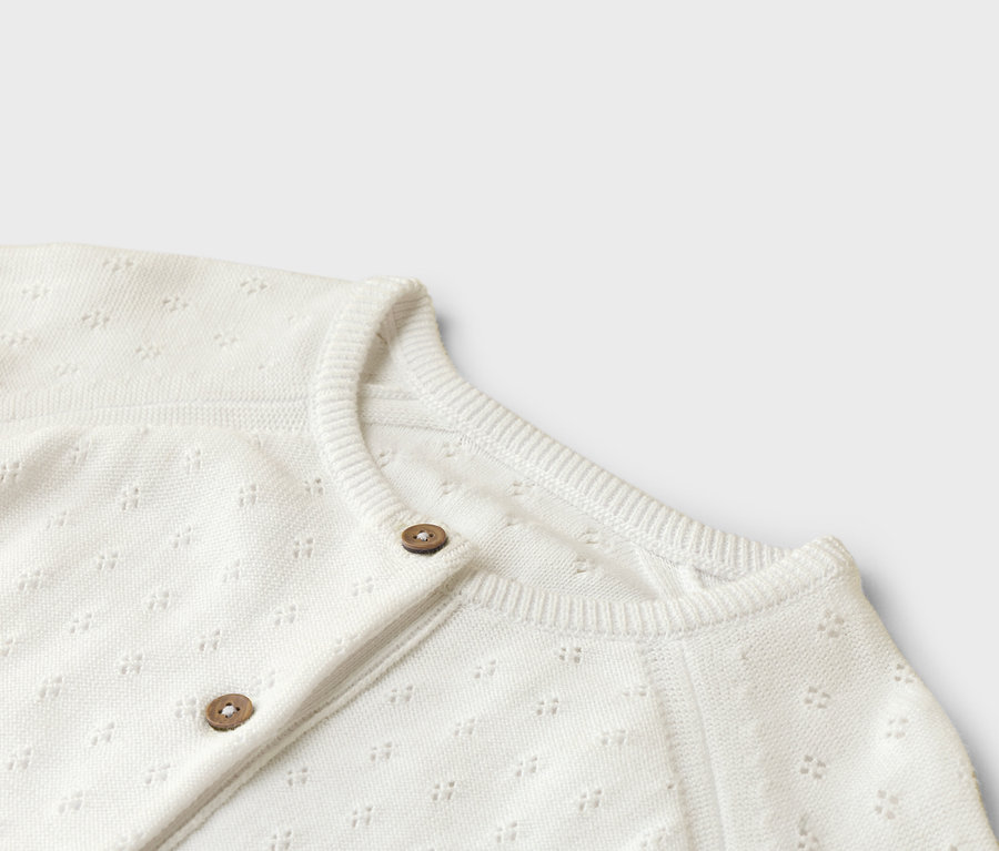 Nahaufnahme einer weißen Strickjacke mit zwei Knöpfen.