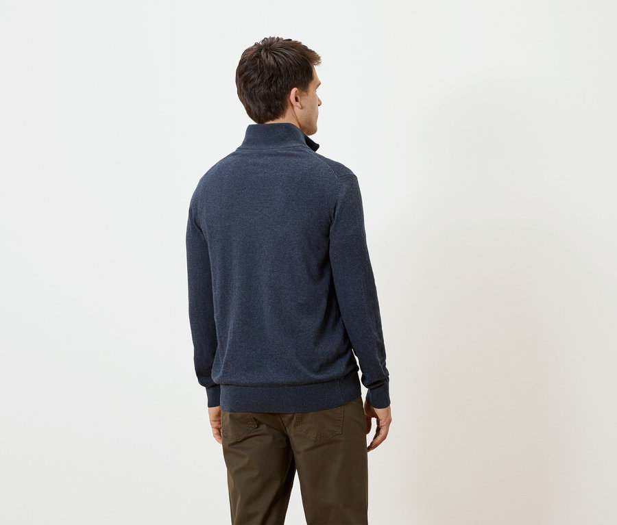 Mann von hinten in marineblauem Pullover und brauner Hose vor weißem Hintergrund.