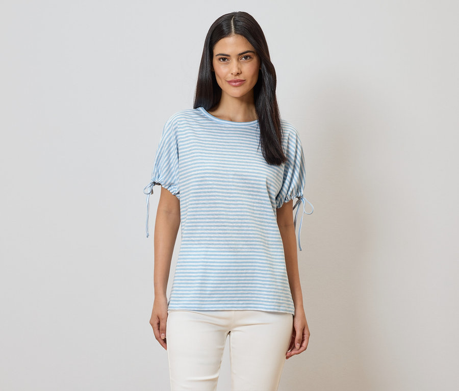 Frau mit blau-weiß gestreiftem T-Shirt mit kurzen Ärmeln und beigen Hosen vor einem hellen Hintergrund.