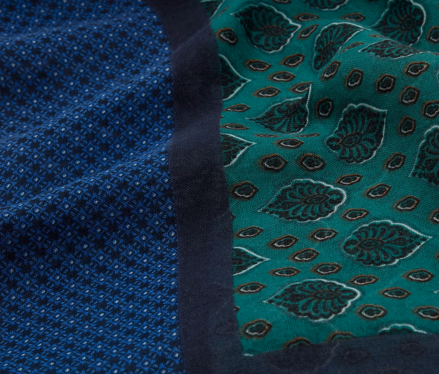 Nahaufnahme von Stoffen mit blauem geometrischen Muster und grünem Blattmuster, getrennt durch einen marineblauen Streifen.