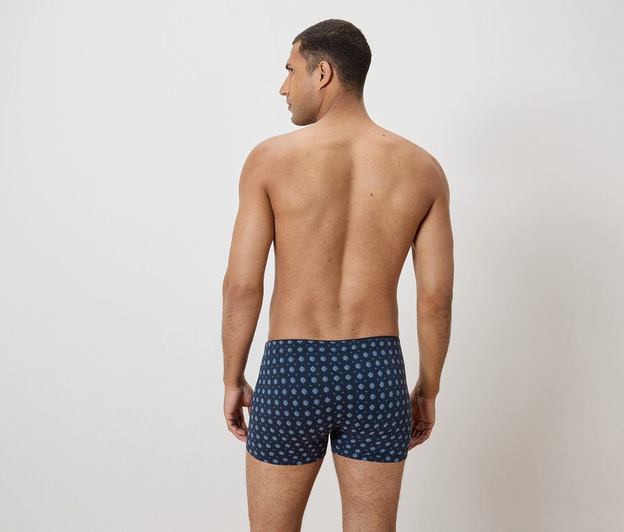 Ein Mann von hinten, der blaue Boxershorts mit Blumenmuster trägt.