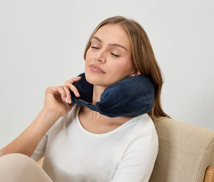 Frau mit geschlossenen Augen trägt eine dunkelblaue Nackenstütze, während sie in einem Sessel sitzt.