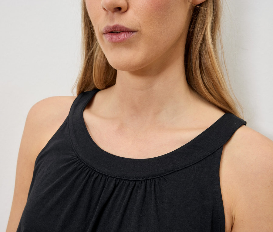Nahaufnahme einer Frau mit blonden Haaren, die ein ärmelloses schwarzes Top trägt.