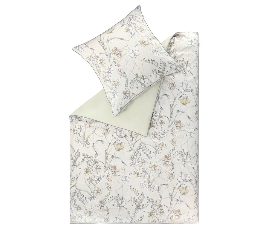 SCHÖNER WOHNEN-Kollektion Bettwäsche »LOVELY« mit floralem Muster. Die Bettdecke ist gefaltet und zeigt eine hellgrüne Rückseite. Das Muster zeigt helle Blüten und grüne Blätter auf hellem Grund. Ein passender Kissenbezug liegt obenauf.