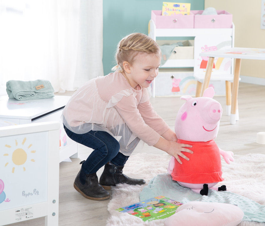 Ein kleines Mädchen spielt mit einem Peppa Pig Stofftier auf einem Teppich.