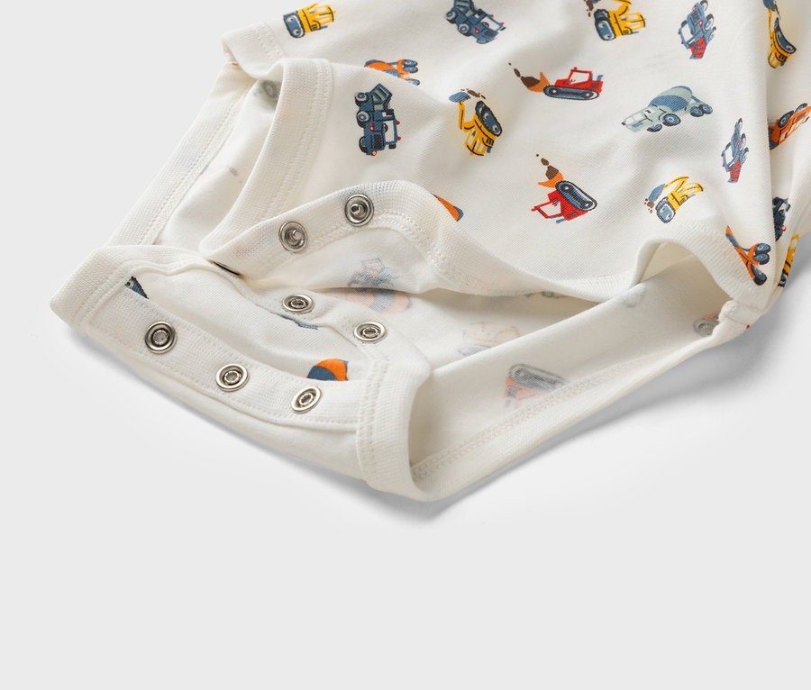 Nahaufnahme eines weißen Babybodys mit einem Muster aus Baufahrzeugen und Druckknöpfen.