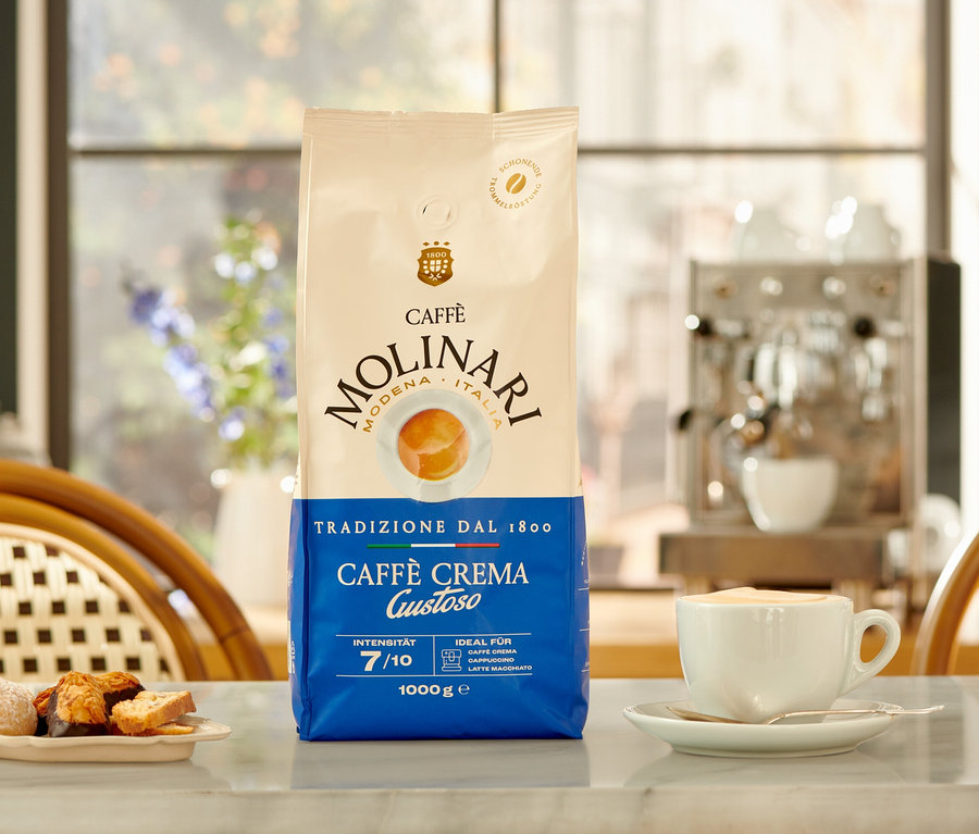 Eine Packung Caffè Molinari Caffè Crema Gustoso, eine Tasse Kaffee und ein Teller Kekse auf einem Tisch.