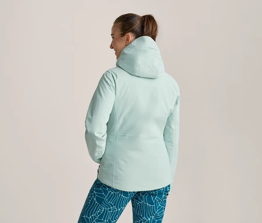 Frau von hinten, trägt eine hellblaue Kapuzenjacke und gemusterte Leggings. Haare zu einem Pferdeschwanz gebunden, blickt leicht nach rechts.