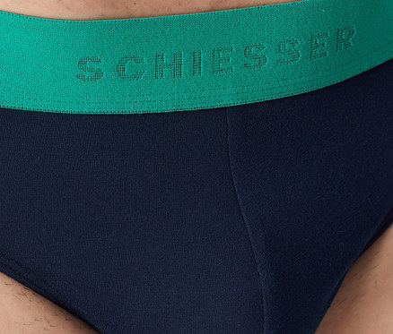 Nahaufnahme einer marineblauen Herrenunterhose mit grünem Bund und „SCHIESSER“-Schriftzug.