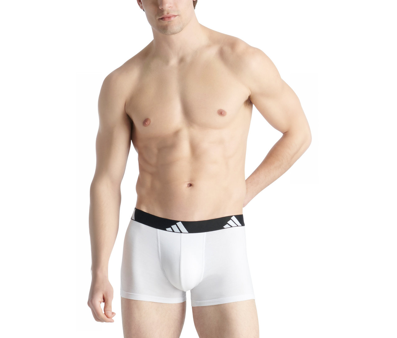 Hemdloser Mann trägt weiße Boxershorts mit schwarzem Bund und weißem Adidas-Logo. Seine linke Hand ruht auf der Hüfte.
