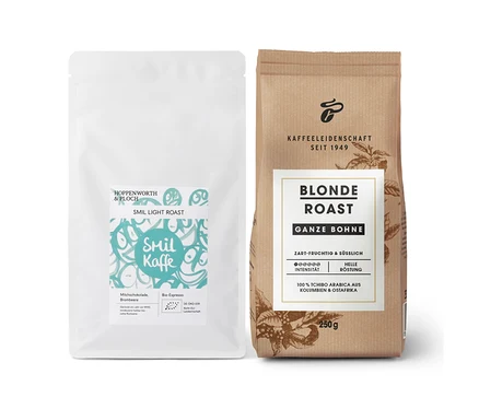Eine weiße Packung Smil Kaffe Light Roast und eine braune Packung Blonde Roast Kaffee, ganze Bohne, stehen nebeneinander.