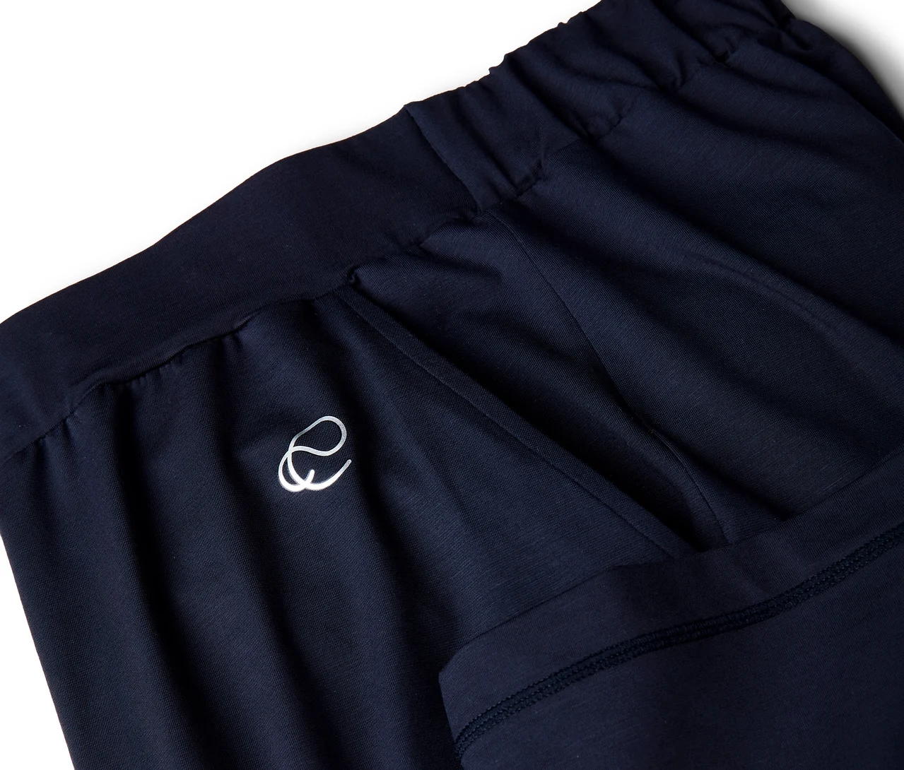 Nahaufnahme einer dunkelblauen Sporthose mit elastischem Bund. Links ist ein weißes stilisiertes 'e'-Logo zu sehen, rechts eine Taschenöffnung.