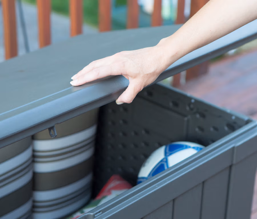 Hand öffnet graue Lifetime-Kissenbox, ca. 440 l, gefüllt mit Kissen und Fußball.
