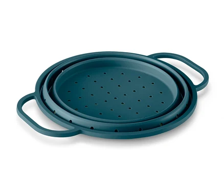 Ein türkisgrünes Silikon-Platzspar-Sieb liegt auf einer weißen Oberfläche.