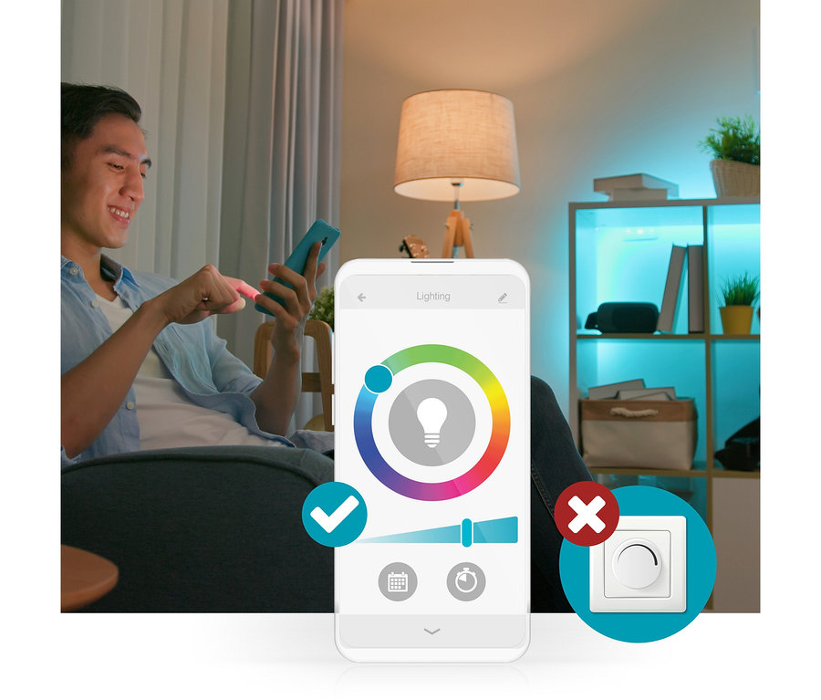 Ein Mann steuert mit einer Smartphone-App die Smart-Beleuchtung; ein blauer Farbton ist auf dem Farbkreis und ein Helligkeitsregler sichtbar. Ein Häkchen bestätigt die App-Steuerung, während ein rotes X einen herkömmlichen Dimmer kennzeichnet.