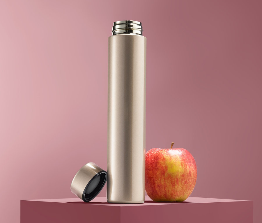 Eine Trinkflasche steht neben einem Apfel, der Deckel liegt daneben.