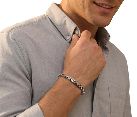 Mann im hellgrauen Hemd, der seinen Kragen berührt und einen Amor Glieder-Armschmuck am Handgelenk trägt.