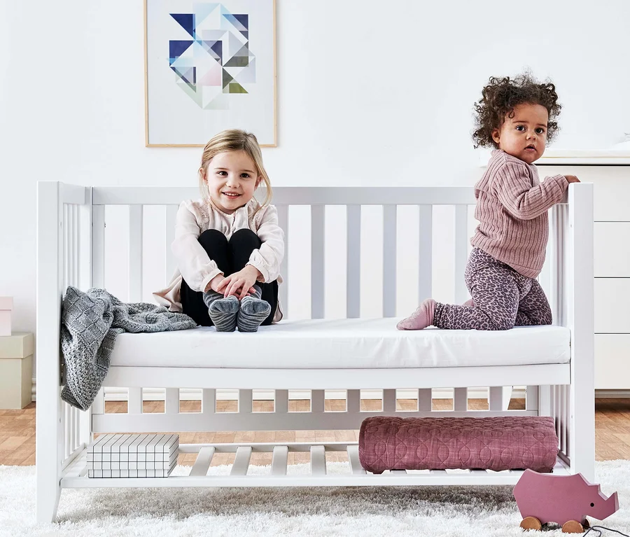 Zwei Kinder sitzen im weißen Hoppekids Babybett »Anton«. Ein Kind sitzt, das andere kniet.