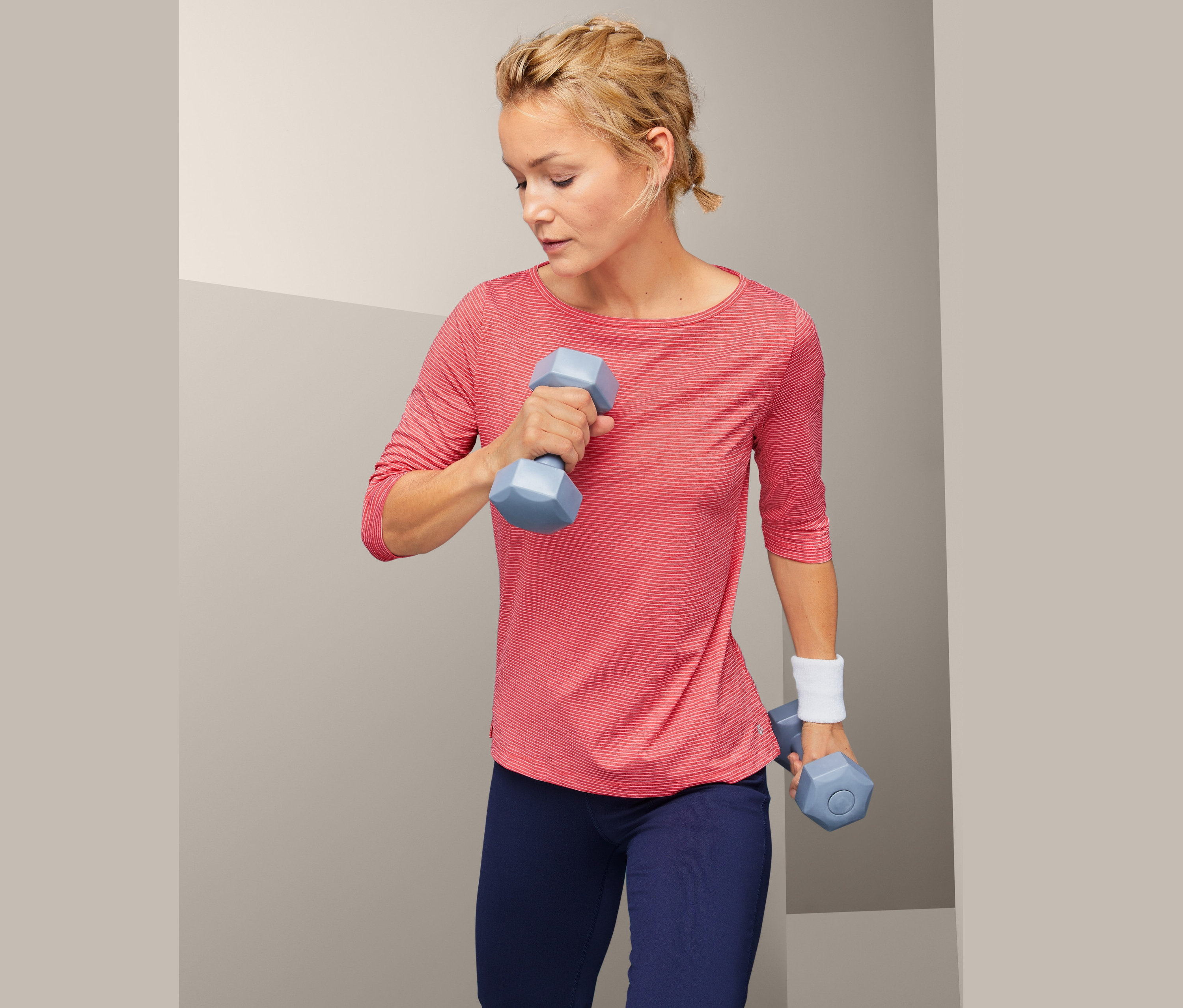 Frau trainiert mit blauen Hanteln und trägt ein Funktionsshirt.