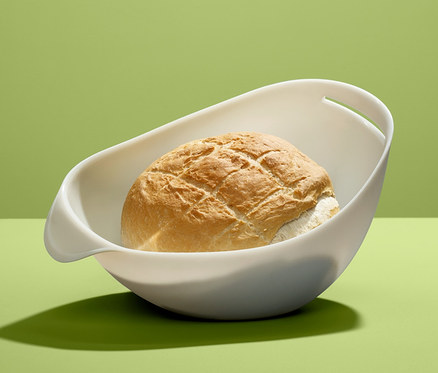 Brotlaib in Brotbackschale vor grünem Hintergrund.