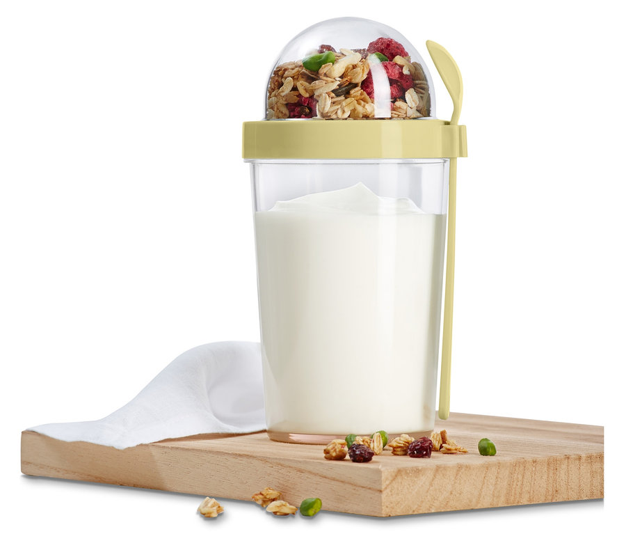 Ein Joghurt-to-go-Becher mit Müsli und Löffel steht auf einem Holzbrett.