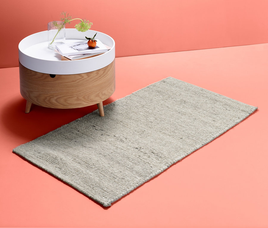 Ein Struktur-Teppich, ca. 140 x 70 liegt neben einem Holztisch mit weisser Tischplatte.