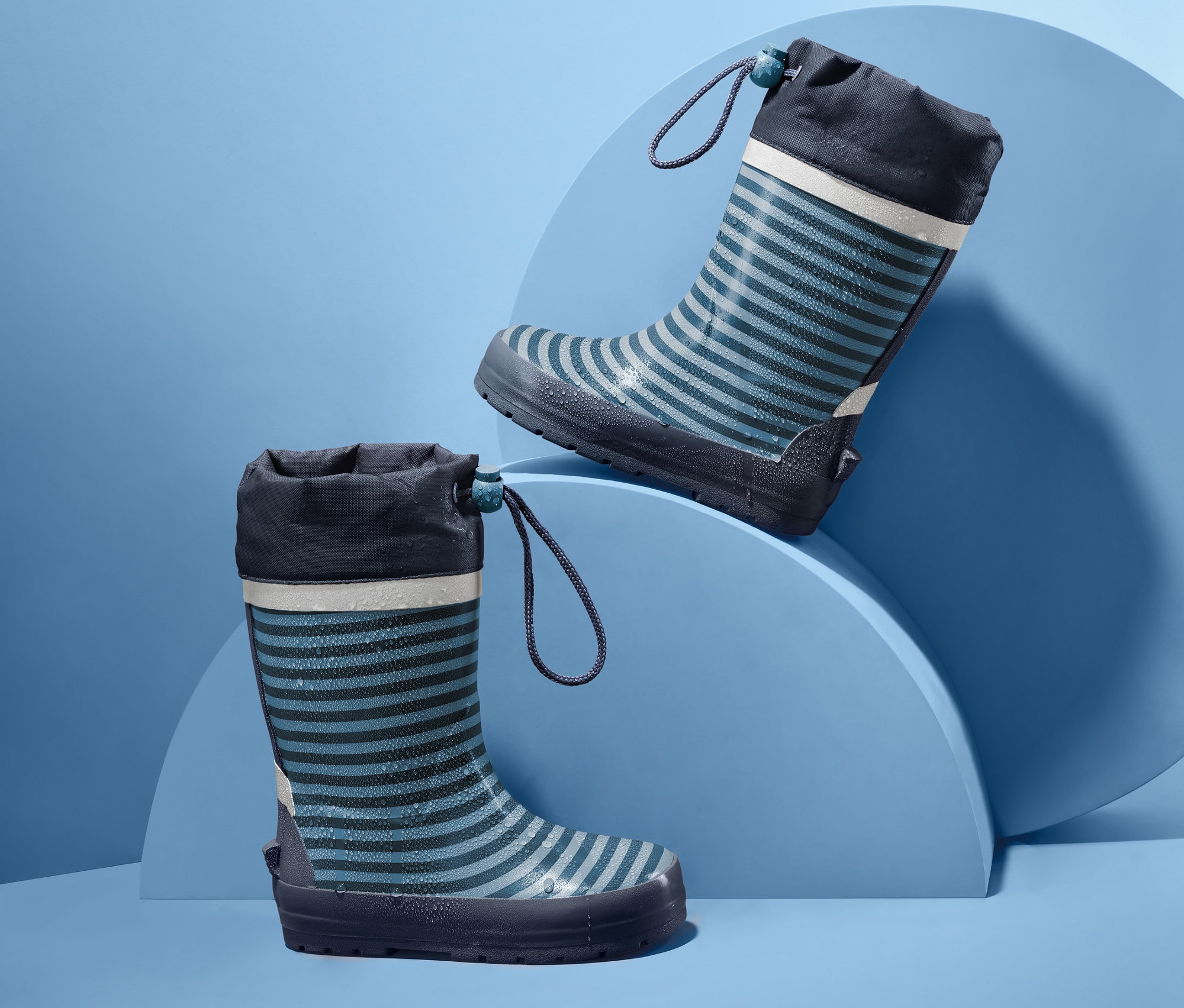 Zwei gestreifte Kinder-Regenstiefel auf blauem Hintergrund.