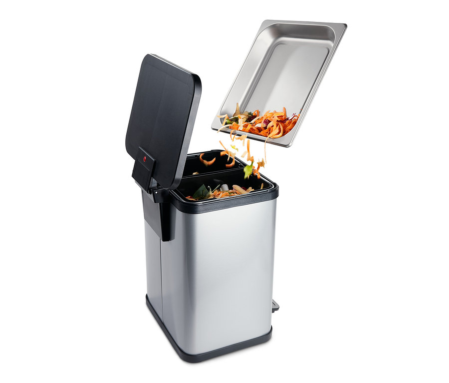 Essensreste fallen aus einer Edelstahlschale in einen silbernen Mülleimer mit schwarzem Deckel.