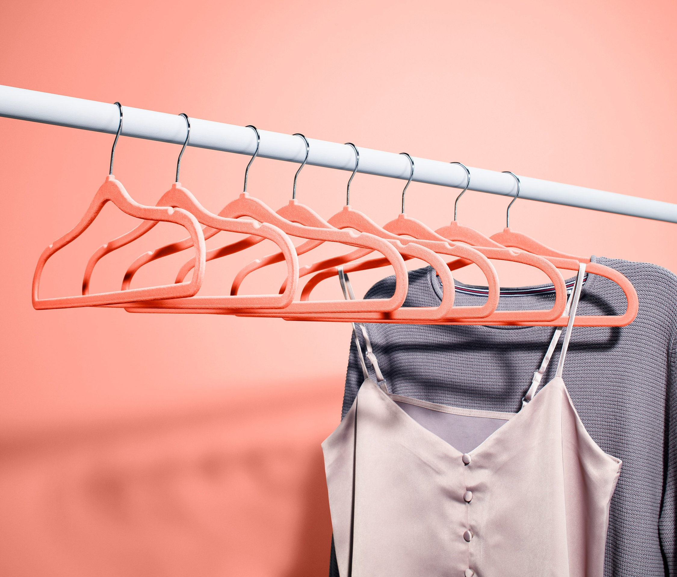 Acht extraschmale Kleiderbügel hängen auf einer weißen Stange. An einem Bügel hängt ein grauer Pullover und ein Top.
