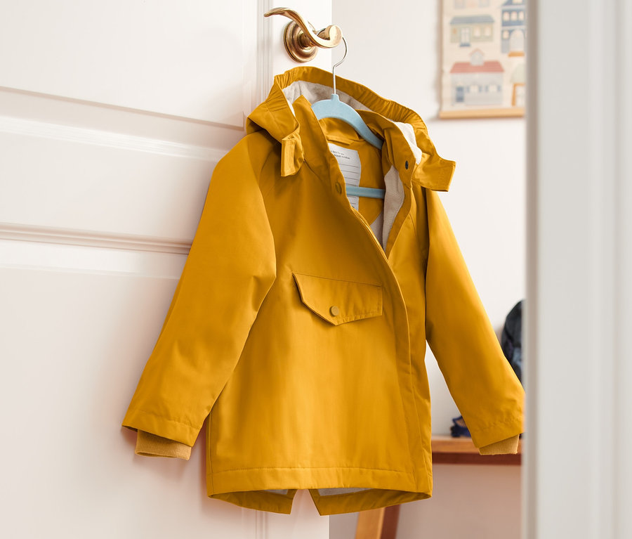 Gelbe Thermo-Regenjacke hängt an einem Türgriff.