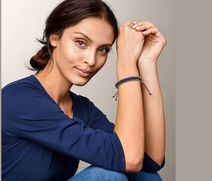 Frau sitzt mit verschränkten Händen, am Handgelenk ein geknüpftes Magnetarmband.
