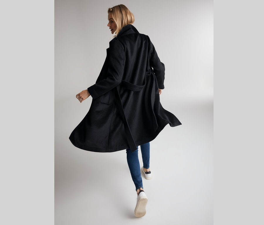 Frau in Jeans und dunkelblauem Mantel aus weicher Wollmischung, die wegschaut.