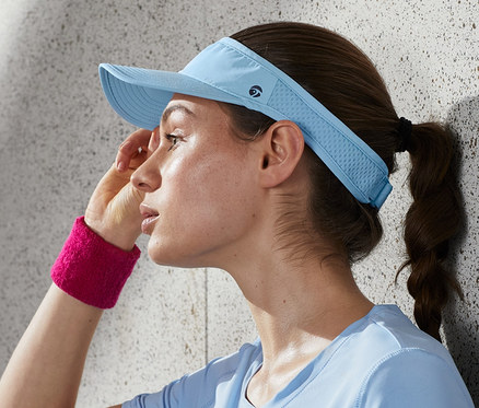 Frau wischt sich Schweiß von der Stirn, trägt ein Laufvisor und ein rosa Schweißband.