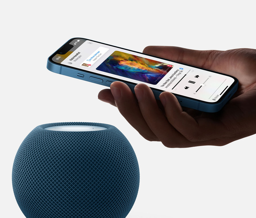 Hand hält blaues iPhone über einem grauen Apple HomePod mini.