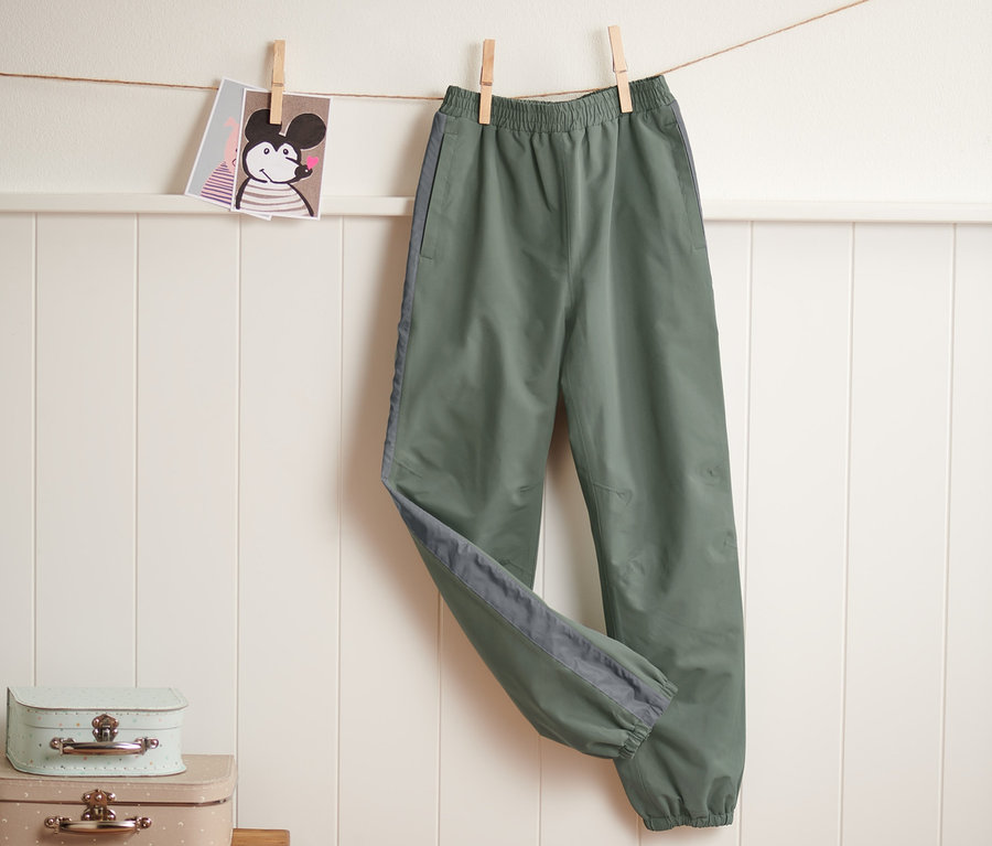 Grüne Regenhose mit reflektierendem Streifen hängt an einer Wäscheleine.