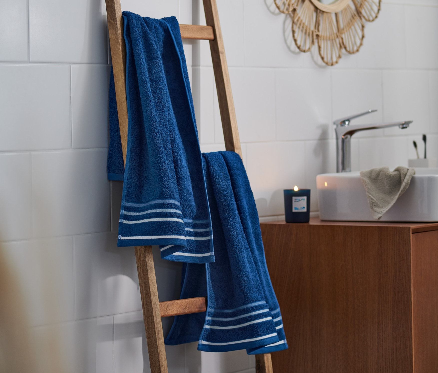 Zwei blaue Handtücher mit Streifen hängen auf einer Holzleiter im Badezimmer.